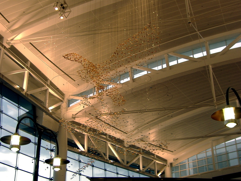 SeaTac, WA: An art form of small golden birds hanging on wires creating a large bird and its reflection inside the SeaTac Intl. Airport