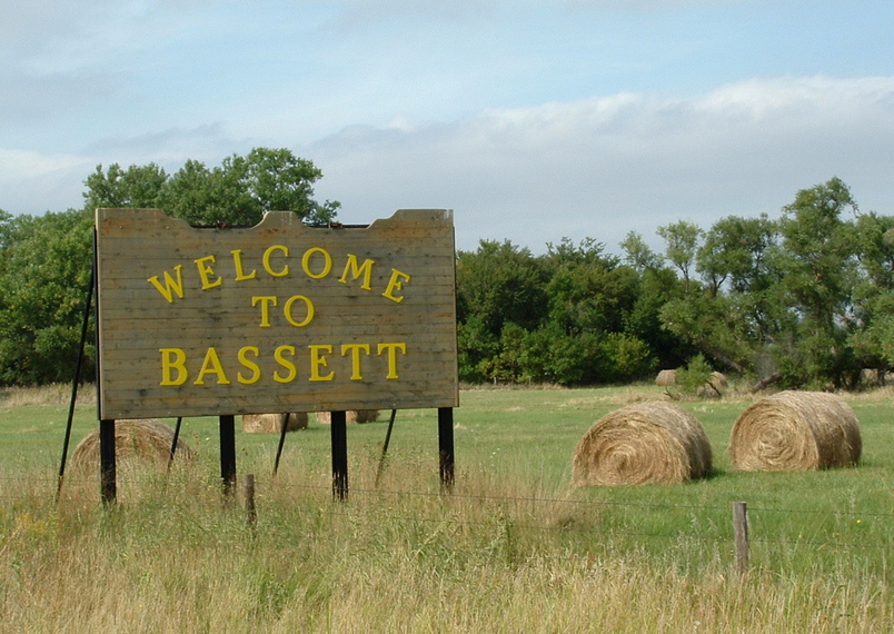 Bassett, NE: This is a picture of the Bassett, NE sign, a strong ranching community, pictured is freshly baled hay.